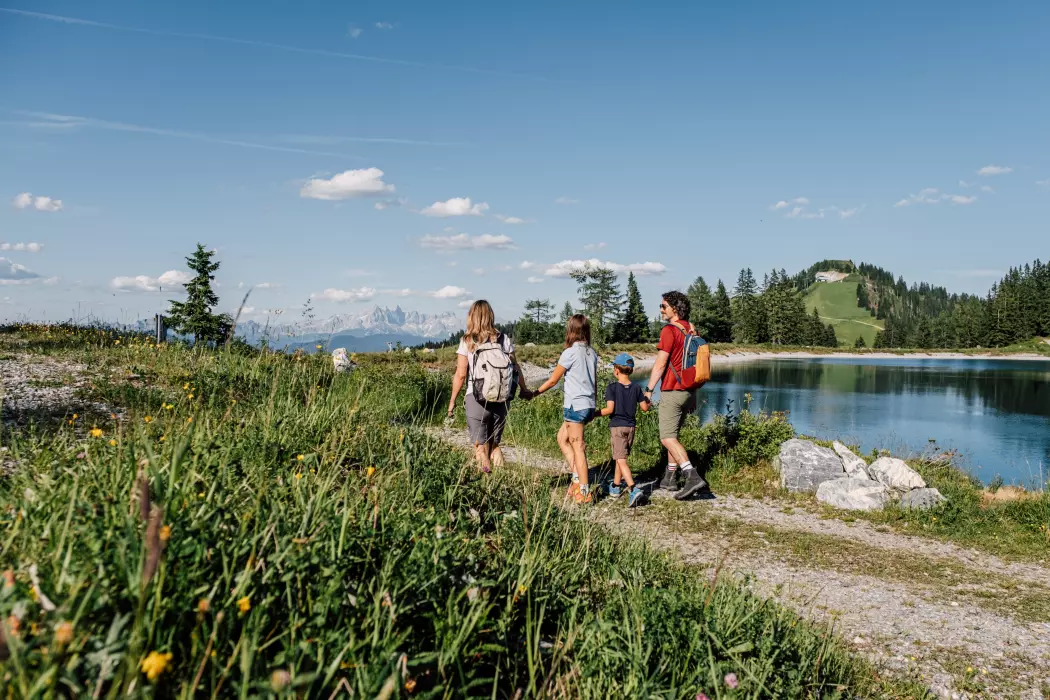 Familie wandert im Sommer auf einem Almweg am Speicherteich in Alpendorf
